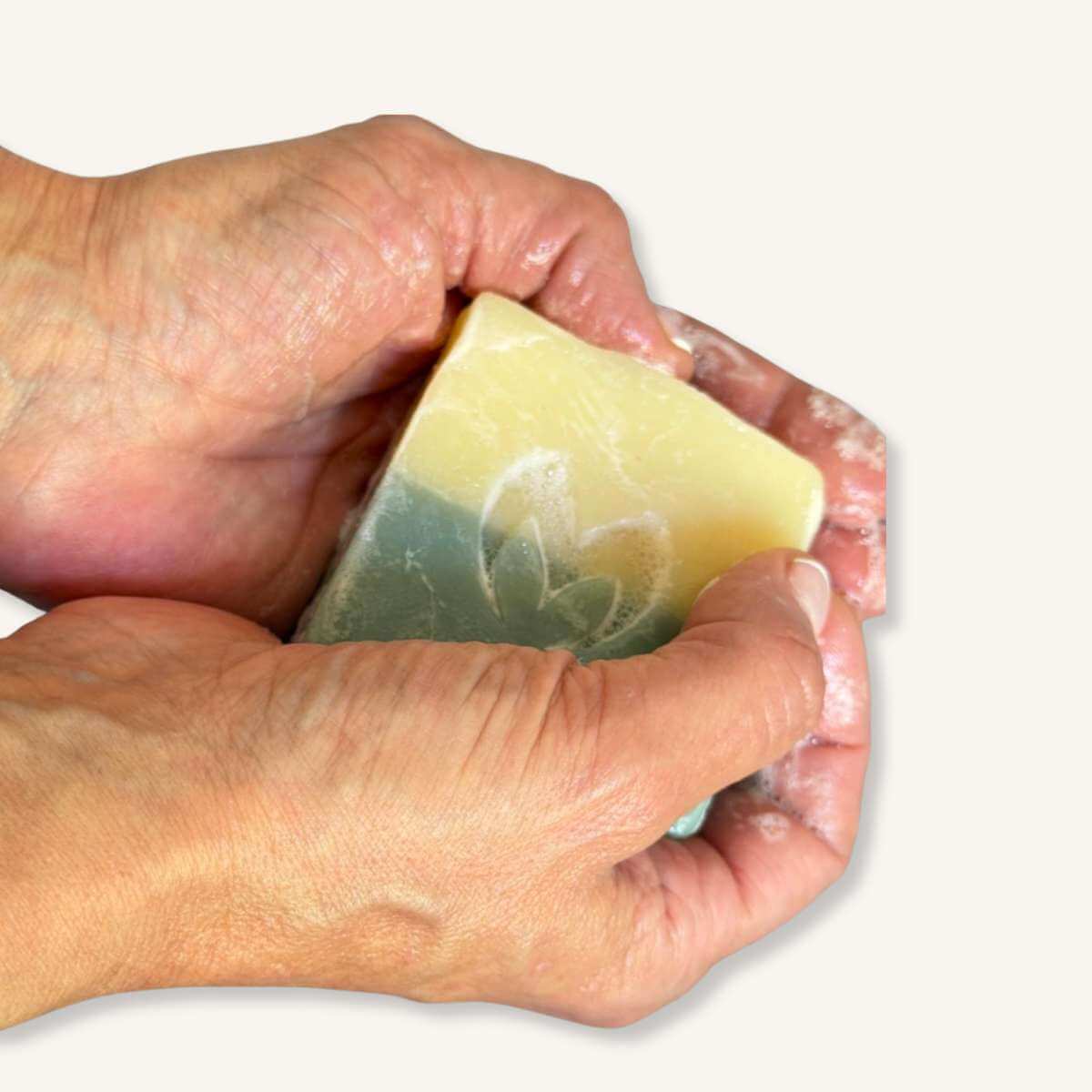 Manos utilizando el jabón artesano de aguacate y mango para mostrar su textura y tamaño real