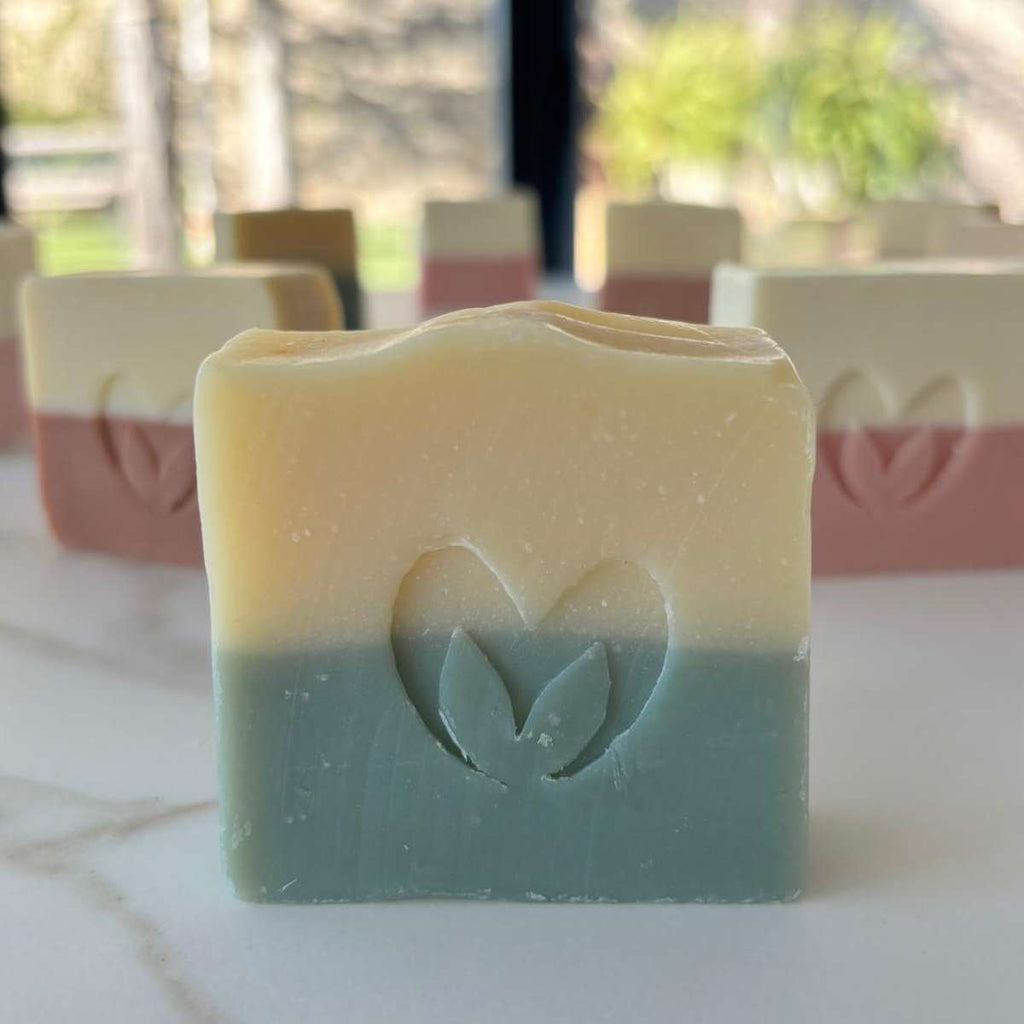  Primer plano de un jabón artesano de aguacate y mango en dos colores con el sello del corazón de Misey grabado, con más jabones al fondo.