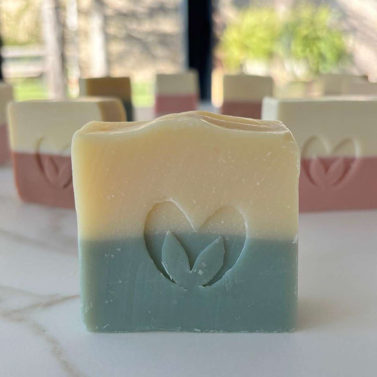  Primer plano de un jabón artesano de aguacate y mango en dos colores con el sello del corazón de Misey grabado, con más jabones al fondo.