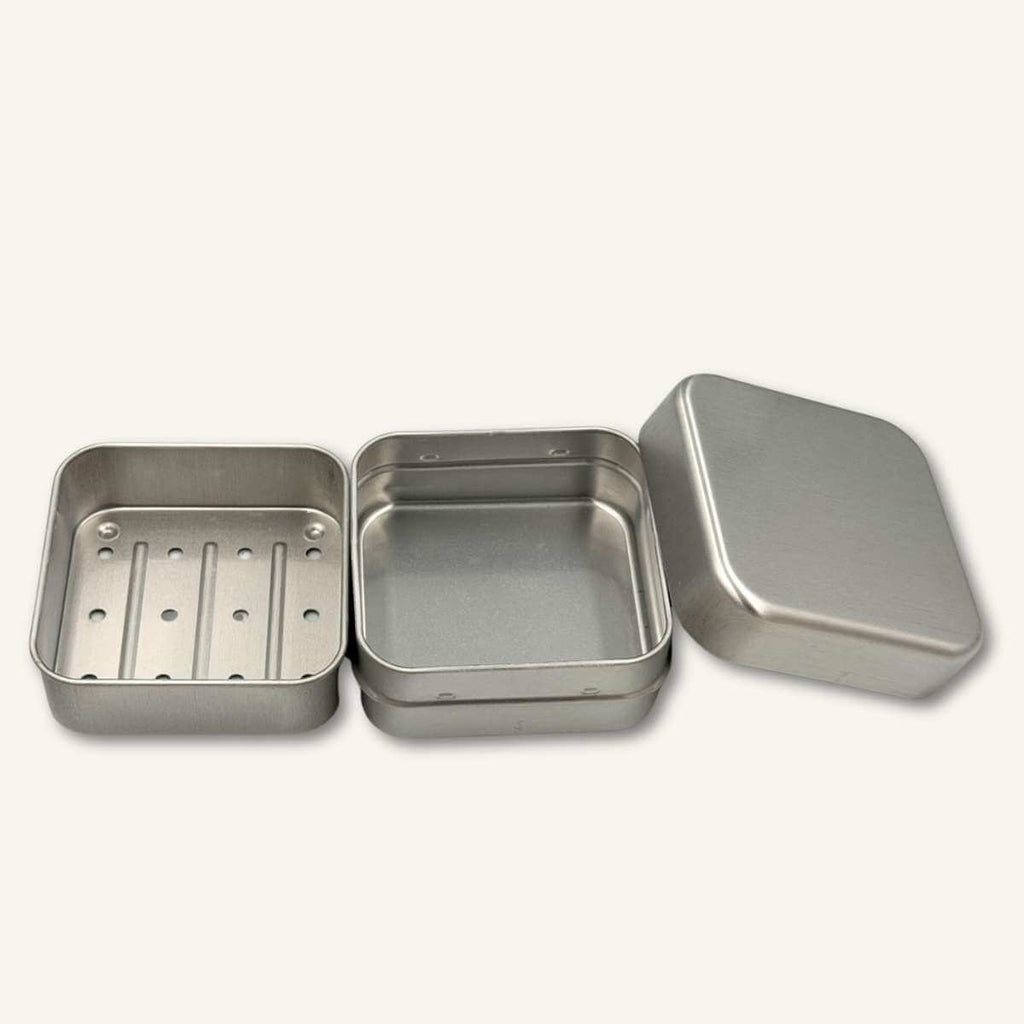 Jabonera de viaje Misey de aluminio inoxidable abierta con rejilla drenante y tapa separada sobre fondo blanco. Cosmética sólida para viajes.